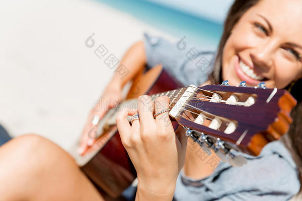 美丽的年幼的女人演奏吉他向海滩