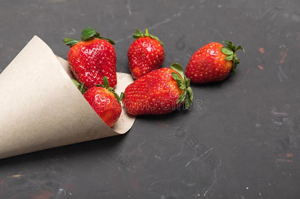 红色的草莓分散的关于纸圆锥体向黑的桌面