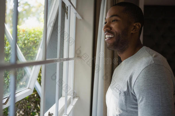 沉思的微笑的男人有样子的出局通过窗在家