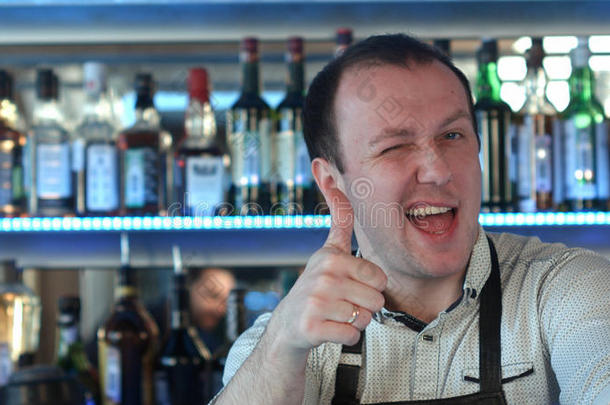酒吧间销售酒精饮料的人起立在指已提到的人柜台微笑的展映他的拇指在上面