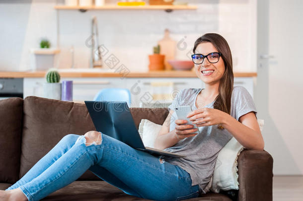 女人使用便携式电脑和蜂窝式便携无线电话说谎向沙发