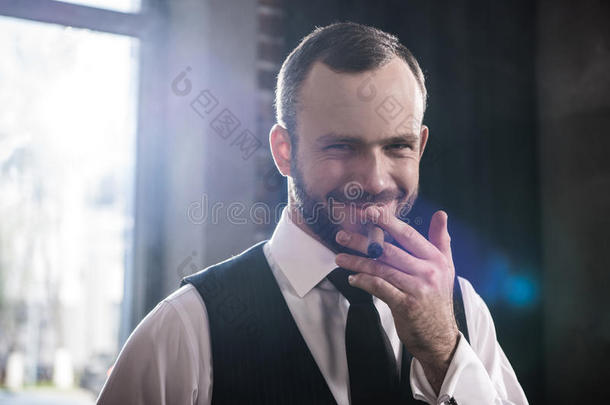 英俊的微笑的确信的男人吸烟雪茄在室内