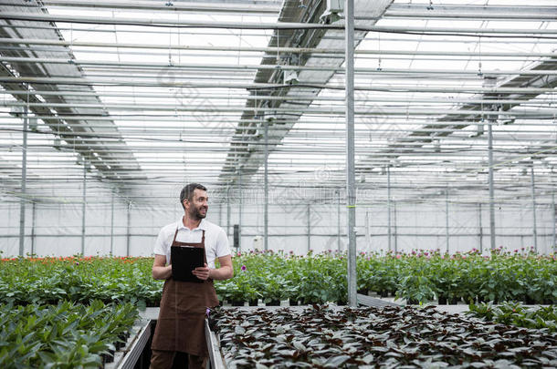 严肃的男人起立采用温室在近处植物hold采用g有纸夹的笔记板