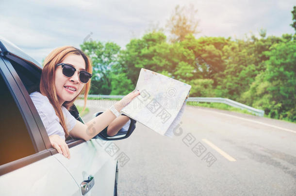 年幼的女人单独的汽车旅行支票和地图向装有向上开的后车门的小轿车汽车