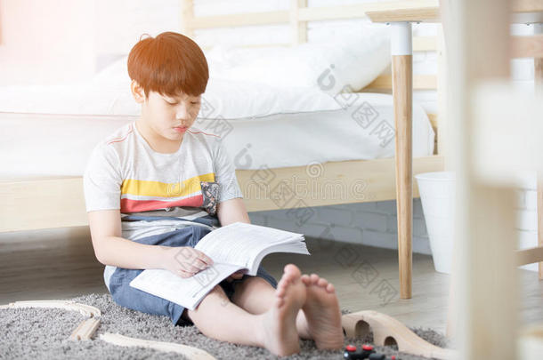 幸福的亚洲人男孩阅读故事书在近处白色的床