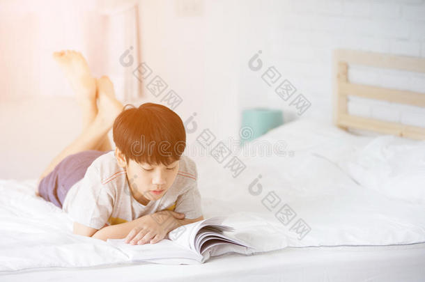 幸福的亚洲人男孩阅读故事书向指已提到的人床
