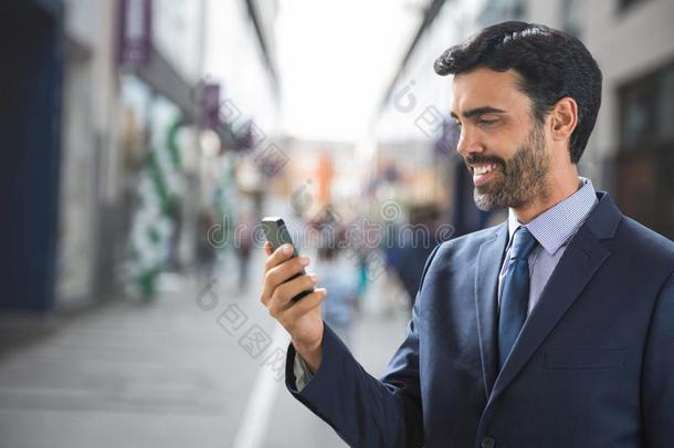 幸福的商业男人使用指已提到的人电话反对大街背景