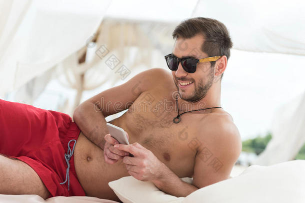 幸福的年轻的男人和胡须发短信经过小玩意向海滩