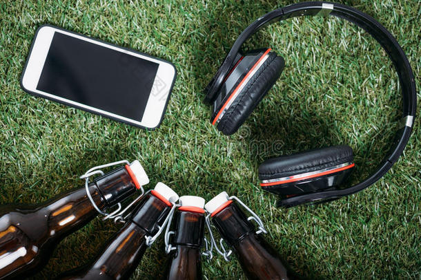 啤酒瓶子和智能手机和耳机说谎向绿色的草