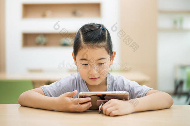亚洲人小孩有样子的在智能手机在图书馆书桌.