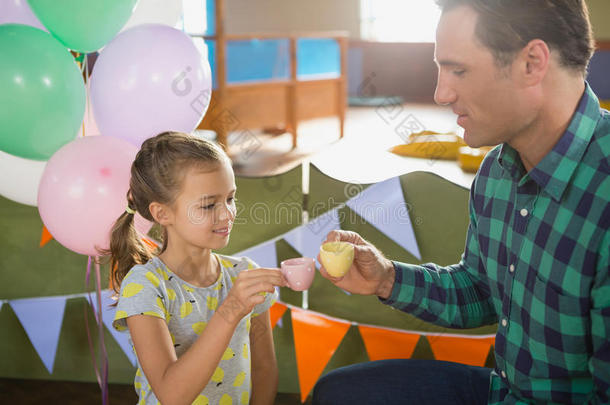 父亲和女孩向祝酒他们的茶水杯子在期间演奏和玩具英语字母表的第11个字母