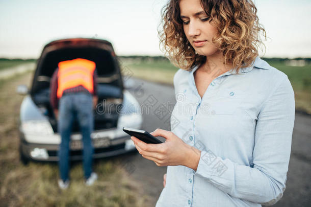 女人调用向服务,男人修理破碎的汽车