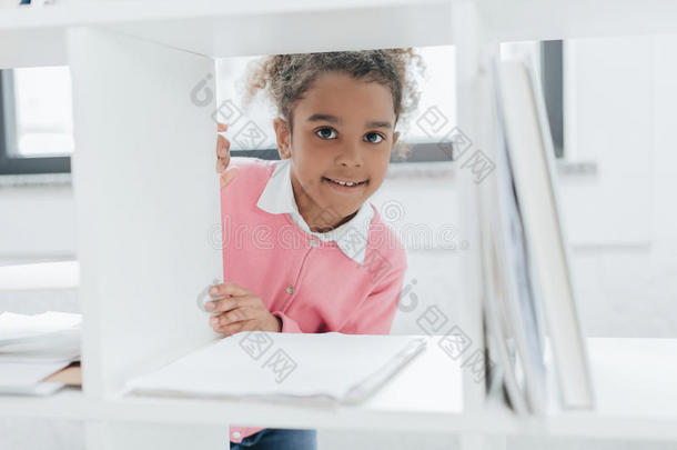 <strong>小</strong>的女孩微笑的在照相机通过<strong>书架</strong>采用办公室
