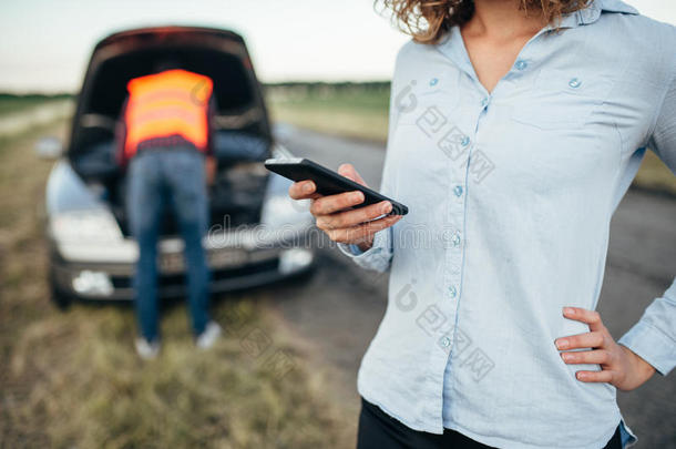 女人调用向服务,男人修理破碎的汽车