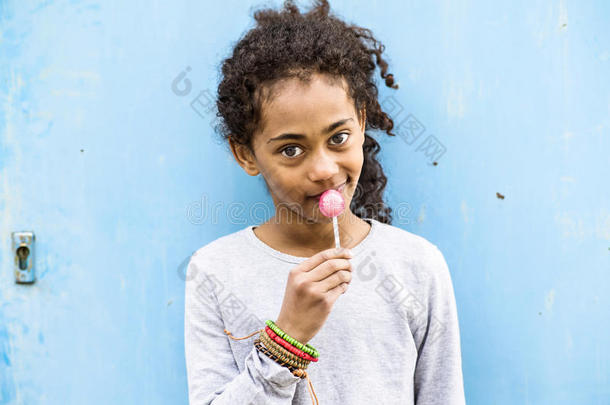 非洲的美国人女孩和有卷发的头发在户外吃棒棒糖.