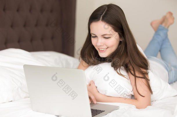 微笑的年幼的女士使用便携式电脑说谎向床,<strong>传达</strong>向li