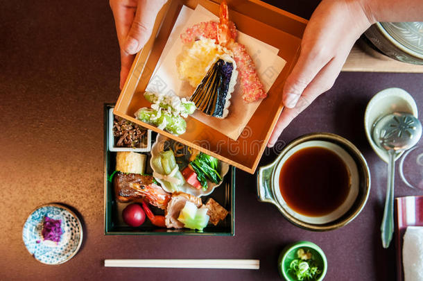 女人手敞开的日本人盒饭或饭盒和烤的海产食品和天麸罗