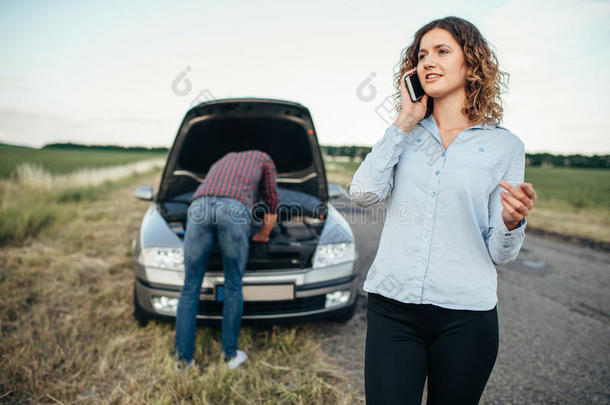 女人调用向服务,男人修理破碎的汽车
