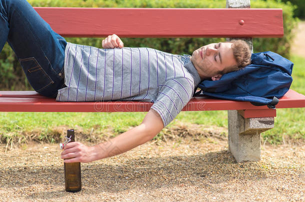 年幼的男人令人轻松的采用一长凳和一瓶子关于啤酒