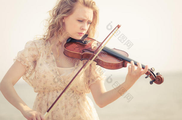 女人演奏小提琴向小提琴在近处海滩