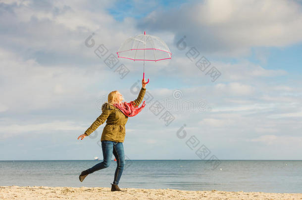 女人用于跳跃的和透明的雨伞向海滩