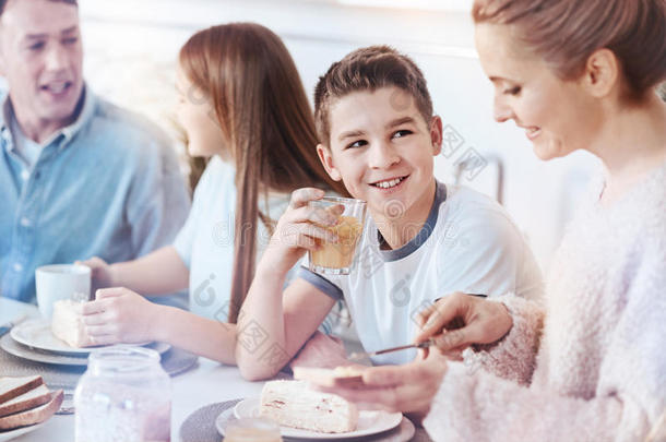 微笑的小的男孩享有桔子果汁在的时候家庭早餐
