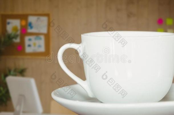 白色的咖啡豆<strong>杯</strong>子向茶<strong>杯托</strong>反对模糊的办公室和黑暗的重叠